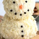 Titled image of a snowman cheeseball on a wooden cutting board with keto crackers around it.