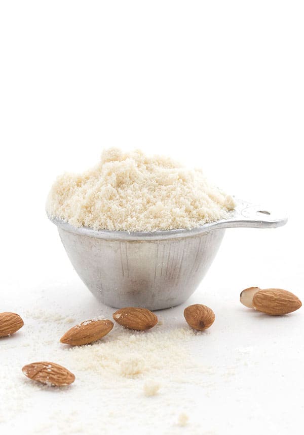 A metal measuring cup filled with almond flour on a white background.