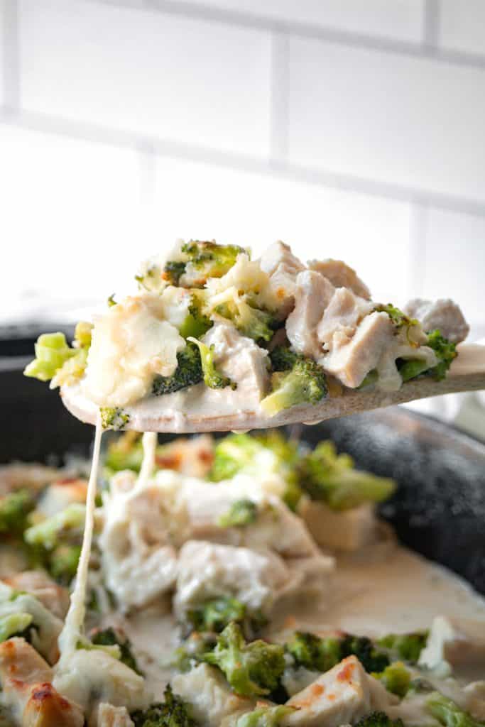 A wooden spoon lifting keto chicken broccoli casserole out of the skillet.