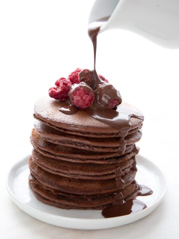 Sugar-free chocolate syrup pouring down over a stack of chocolate protein pancakes.