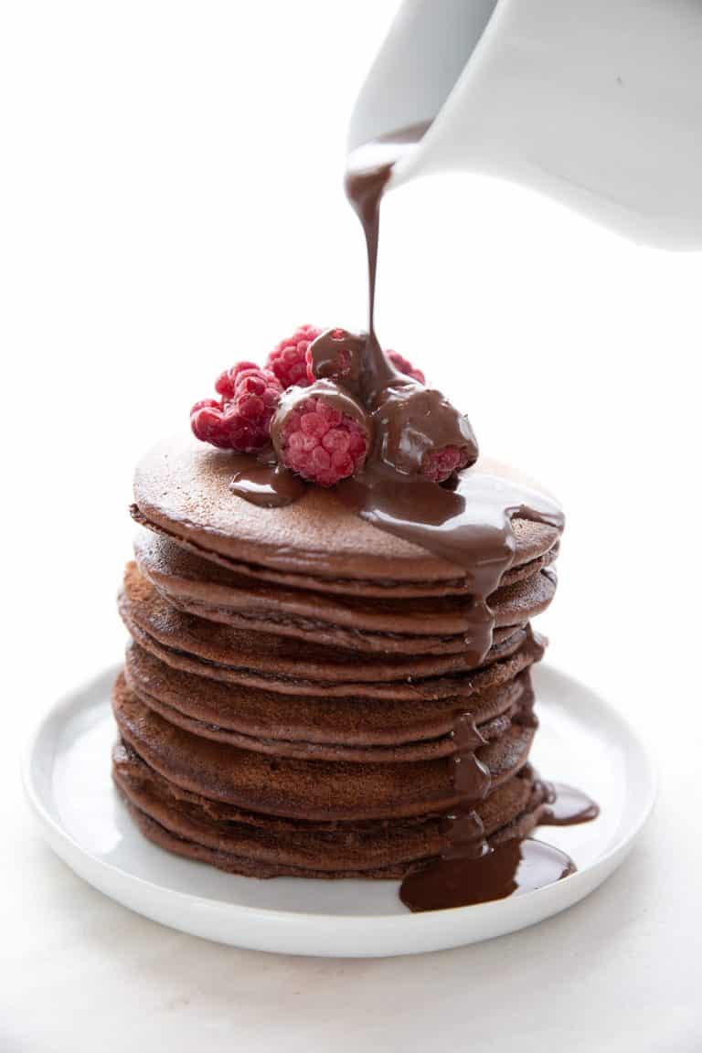 Sugar-free chocolate syrup pouring down over a stack of chocolate protein pancakes.