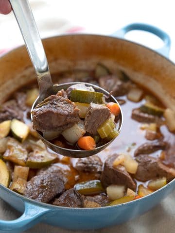 A ladle full of keto beef stew being lifted out of the Dutch oven.