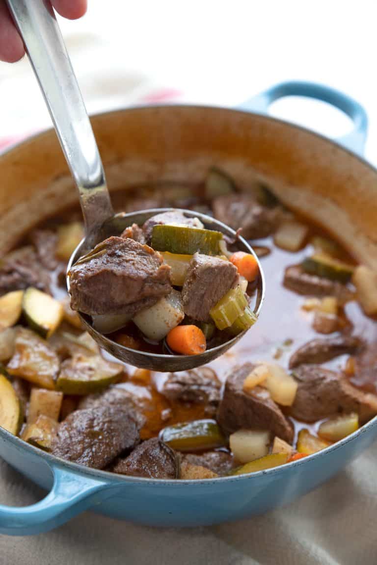 A ladle full of keto beef stew being lifted out of the Dutch oven.