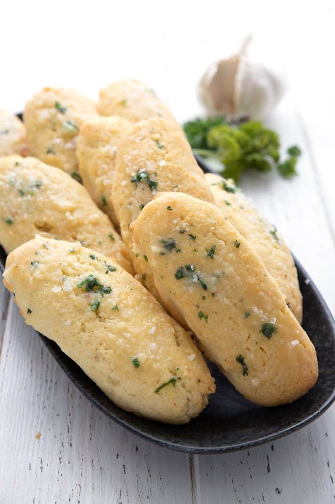 Keto Breadsticks lined up on a black plate with garlic and parsley in the background.