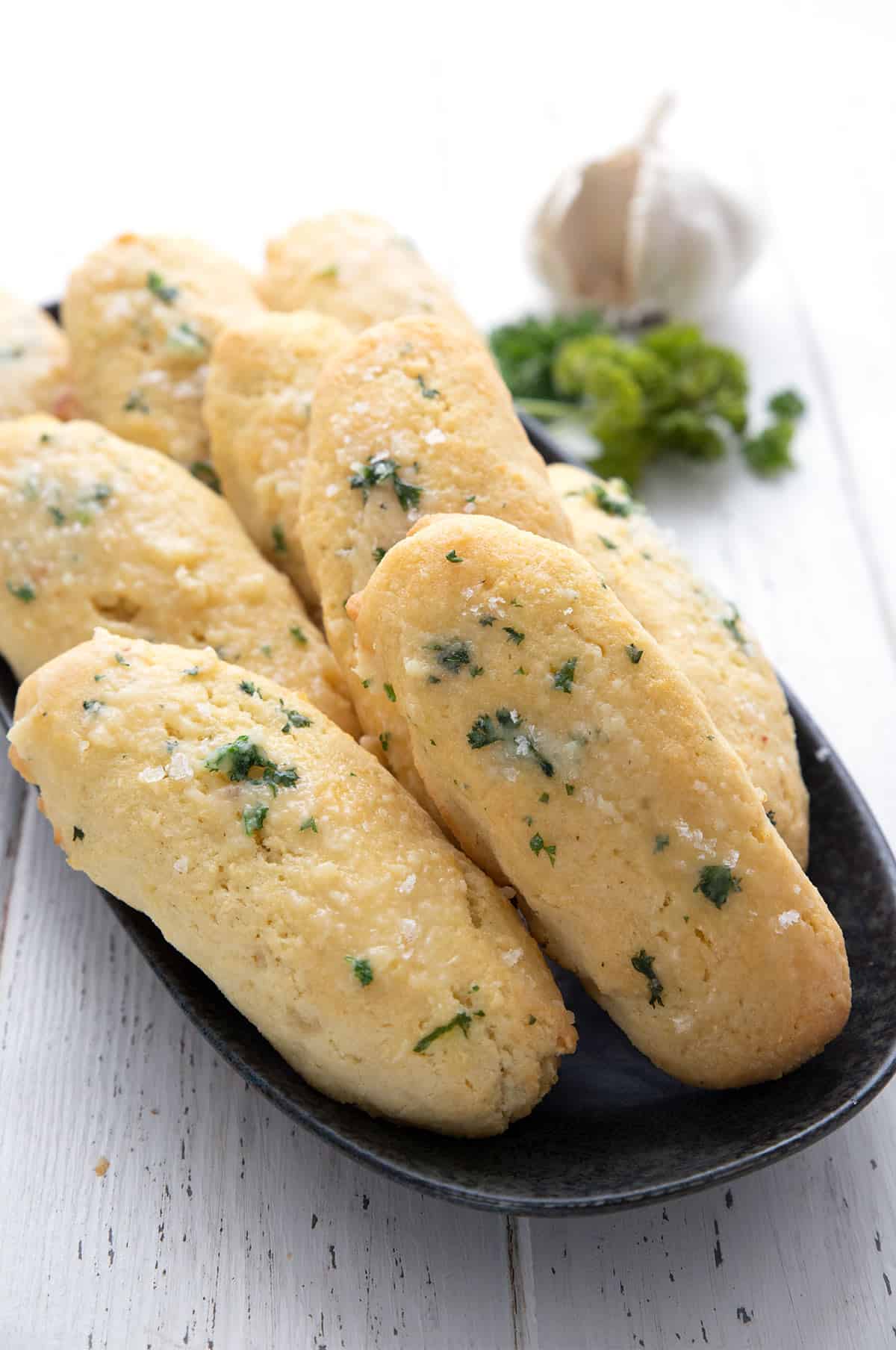 Keto Breadsticks lined up on a black plate with garlic and parsley in the background.
