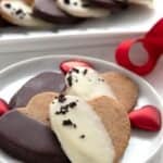 Hearth shaped keto espresso shortbread cookies, half dipped in white or dark chocolate, piled up on a white plate with red ribbon in the background.