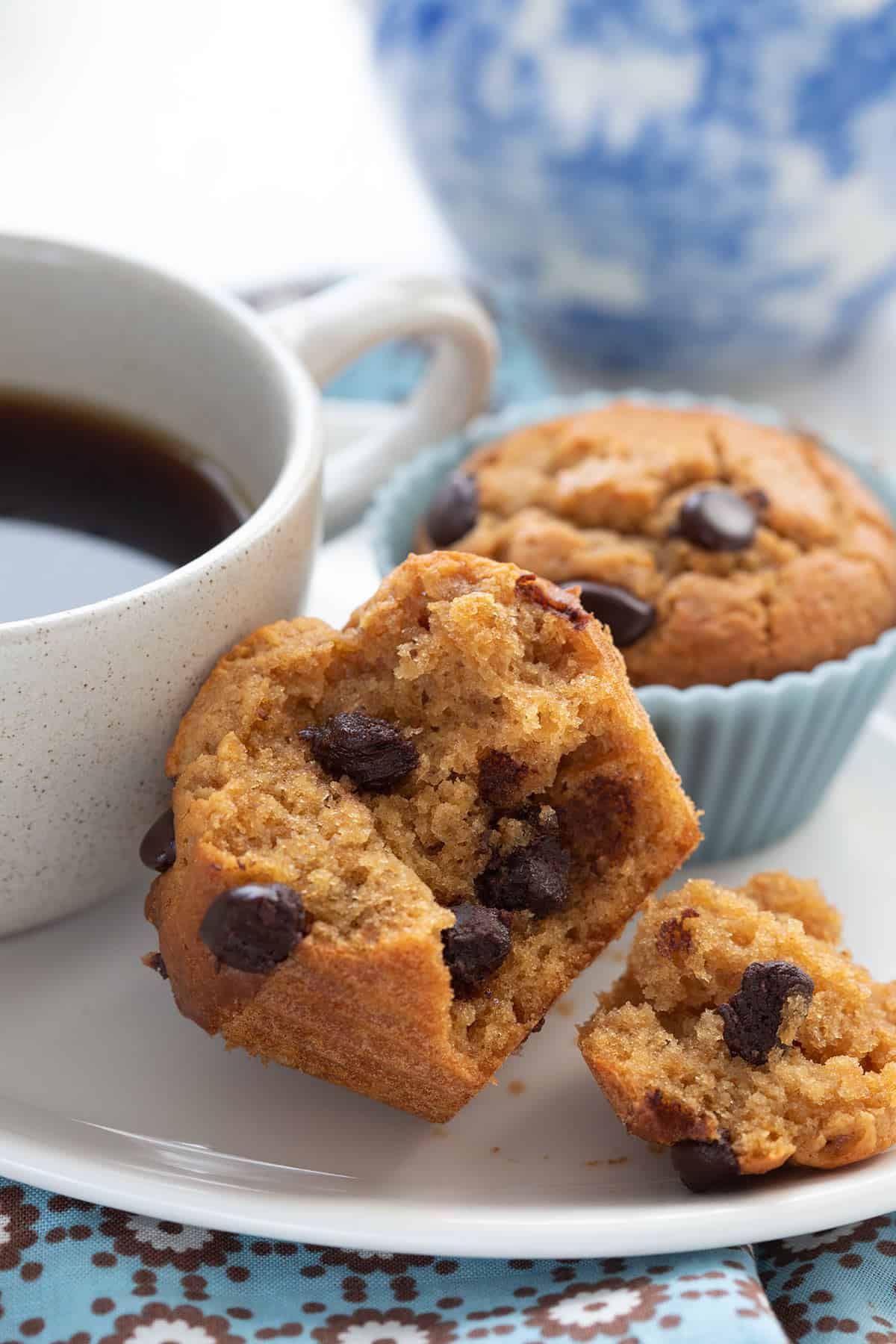 Close up shot of a flourless keto peanut butter muffins with a cup of coffee and a blue vase in the background.