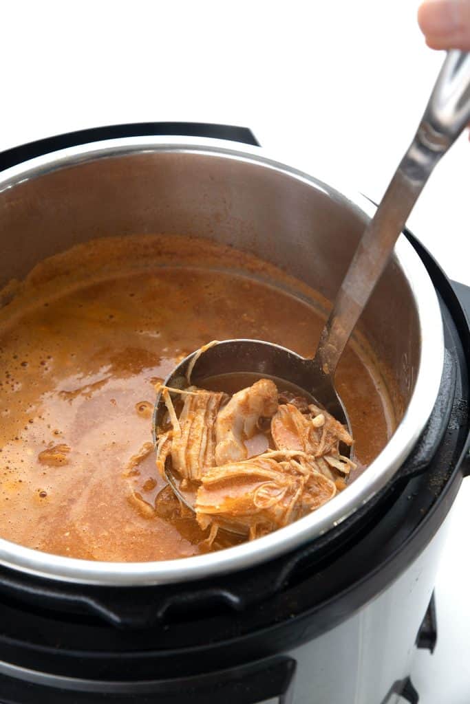 A ladle lifting shredded chicken out of an Instant Pot full of chicken enchilada soup.