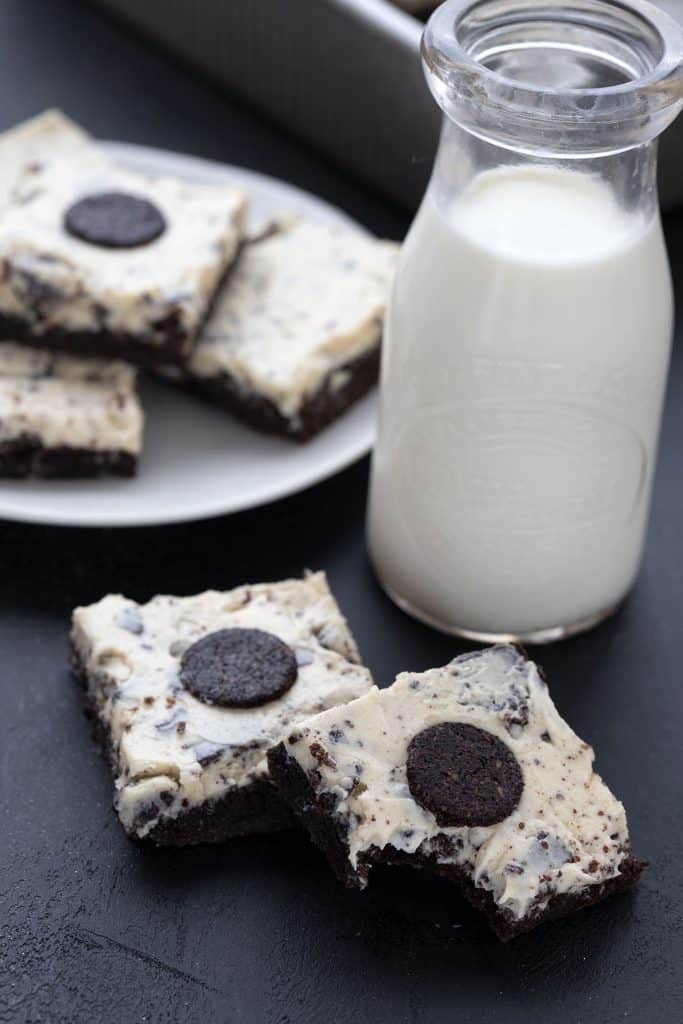 Two keto oreo brownies on a black table, with a glass bottle full of milk.