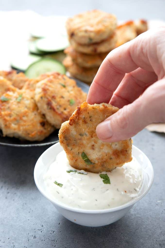 A hand dipping a chicken fritter into ranch dressing.