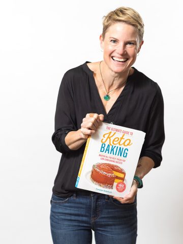Carolyn Ketchum laughing, holding a copy of The Ultimate Guide to Keto Baking.