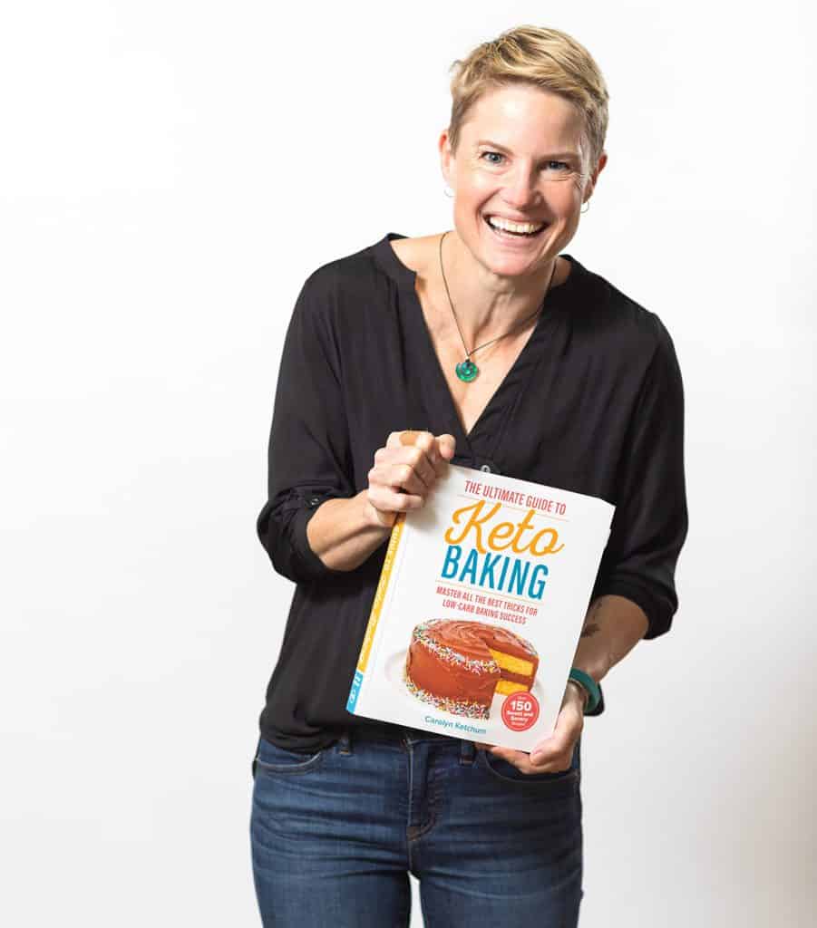 Carolyn Ketchum laughing, holding a copy of The Ultimate Guide to Keto Baking.