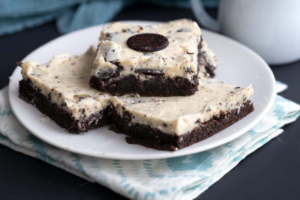 Keto cookies and cream brownies on a white plate over a patterned napkin.