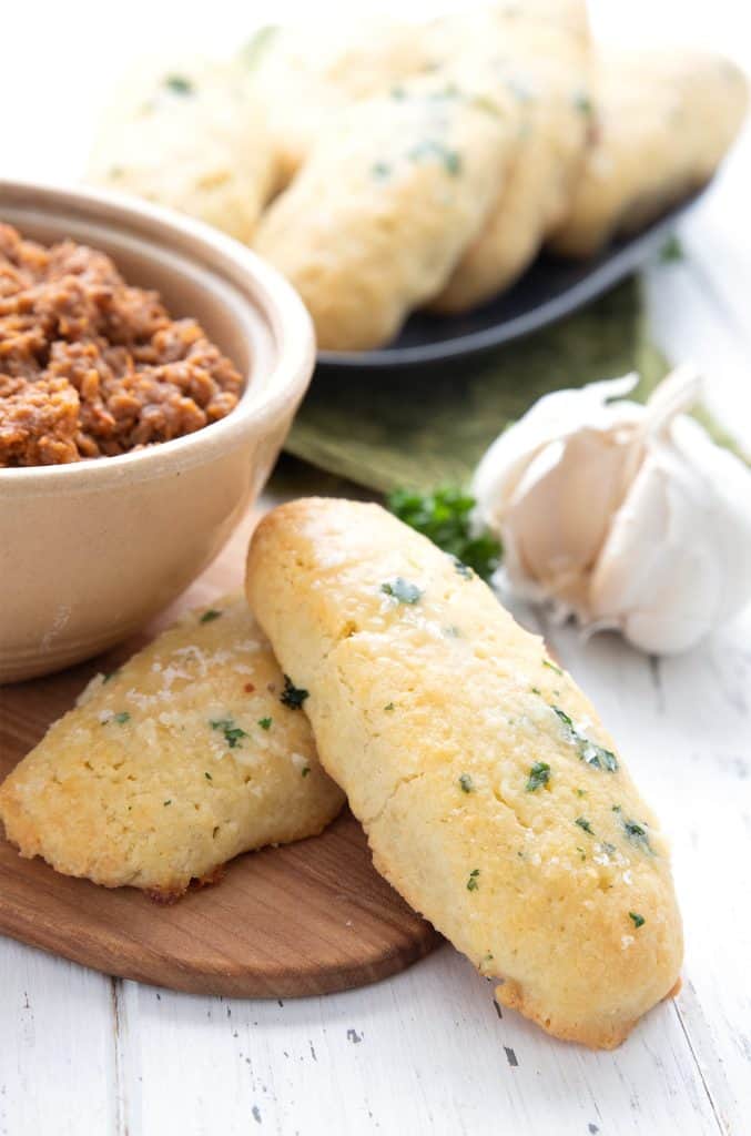 Two keto breadsticks on a cutting board beside a bowl of chili.