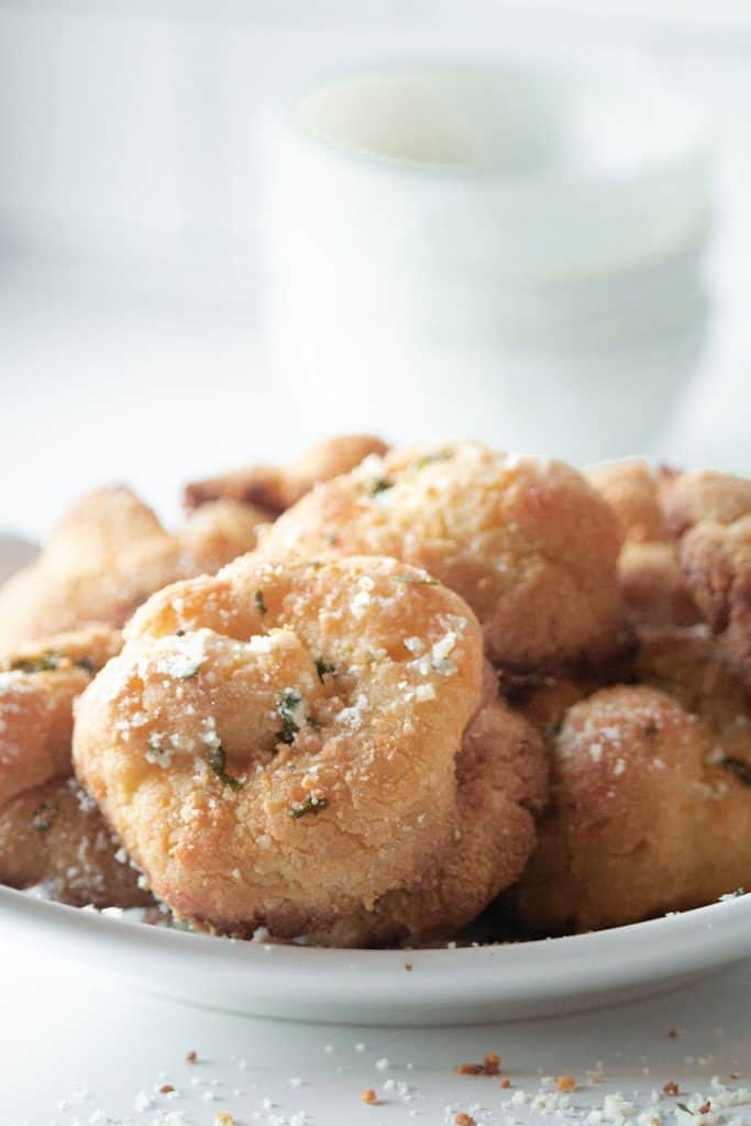 A white bowl full of keto garlic knots with crumbs strewn around.
