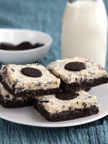 Cookies and cream brownies on a teal coloured cloth with a bottle of milk in the background.