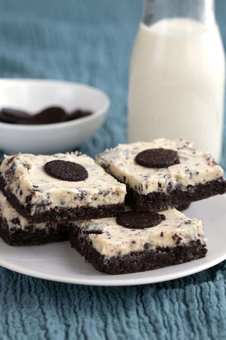 Cookies and cream brownies on a teal coloured cloth with a bottle of milk in the background.