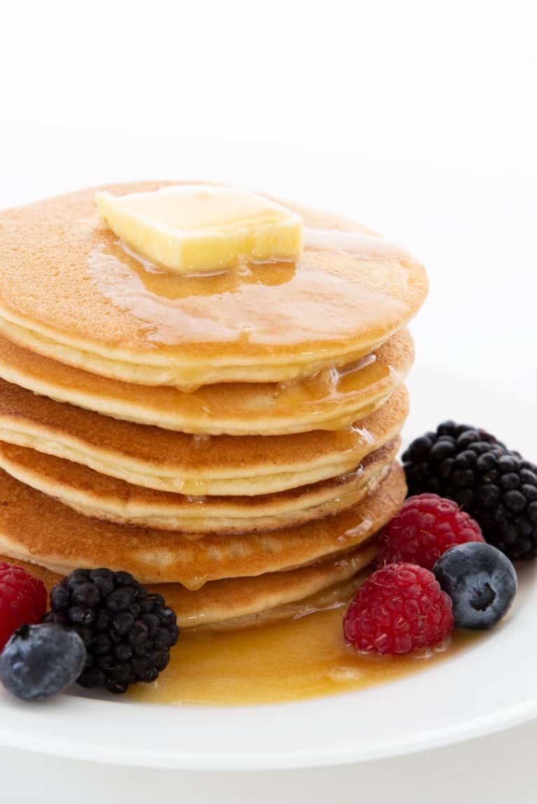 A stack of keto pancakes with a pat of butter melting on top, surrounded by fresh berries.