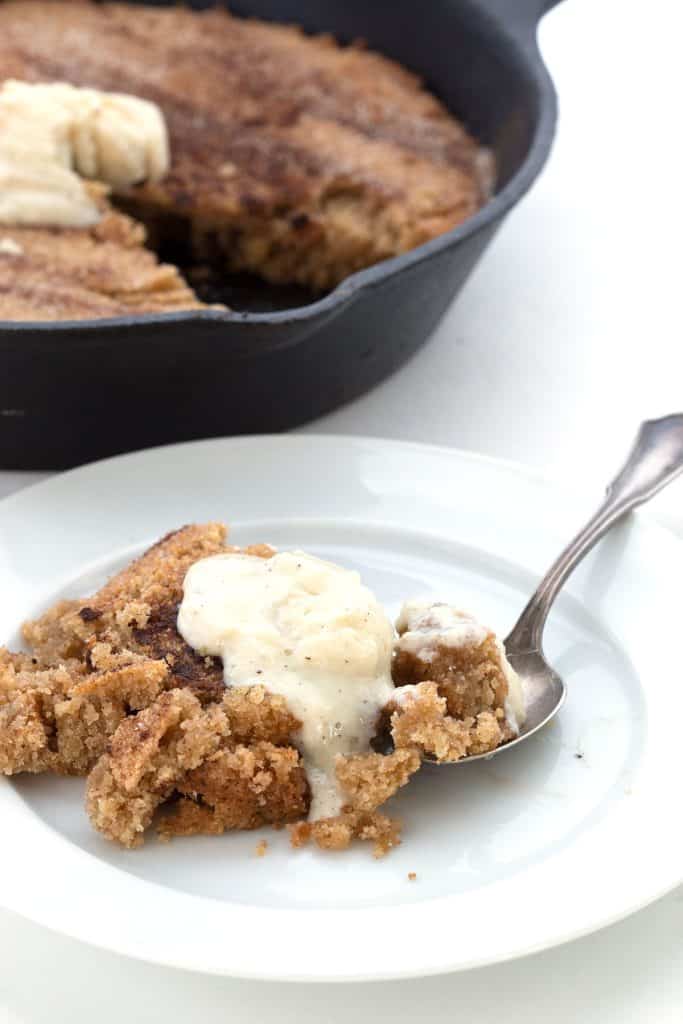 A white plate with a serving of warm keto snickerdoodle cookie, with ice cream melting on top.