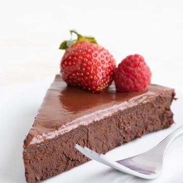 A slice of dairy-free keto flourless chocolate cake on a white plate with two berries on top.