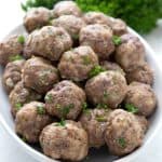 A serving dish filled with keto meatballs, with a bunch of parsley in the background.