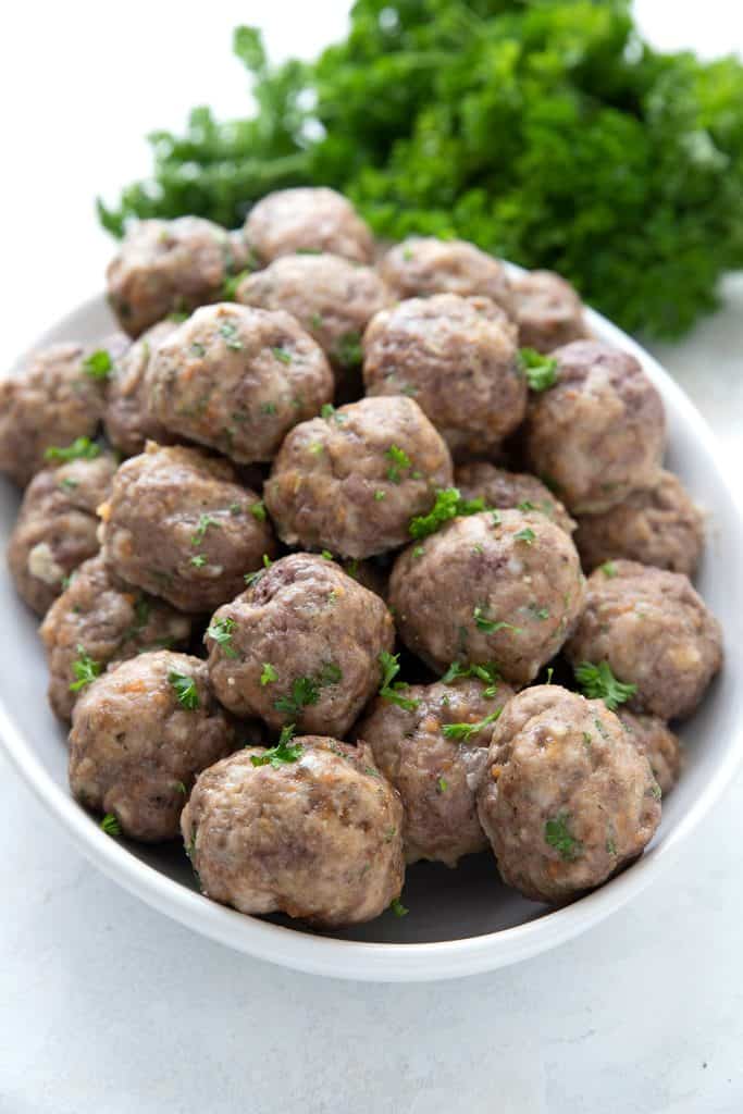 A serving dish filled with keto meatballs, with a bunch of parsley in the background.