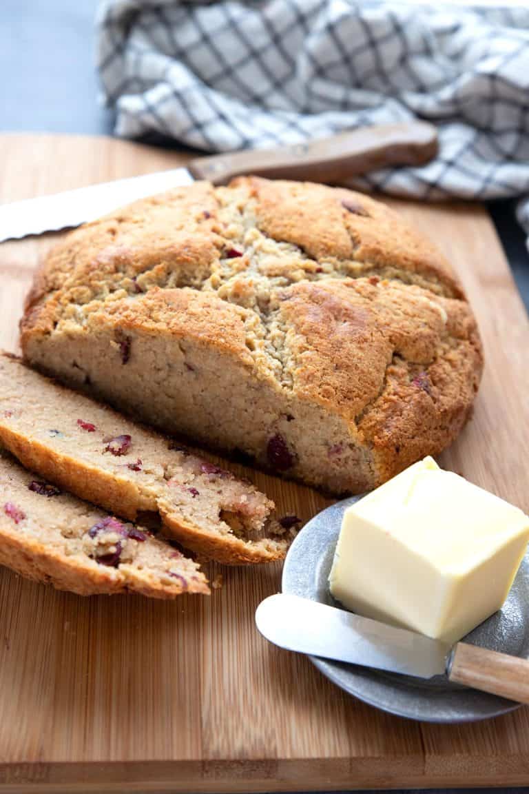 A loaf of keto Irish soda bread on a wooden cutting board with a small plate of butter.