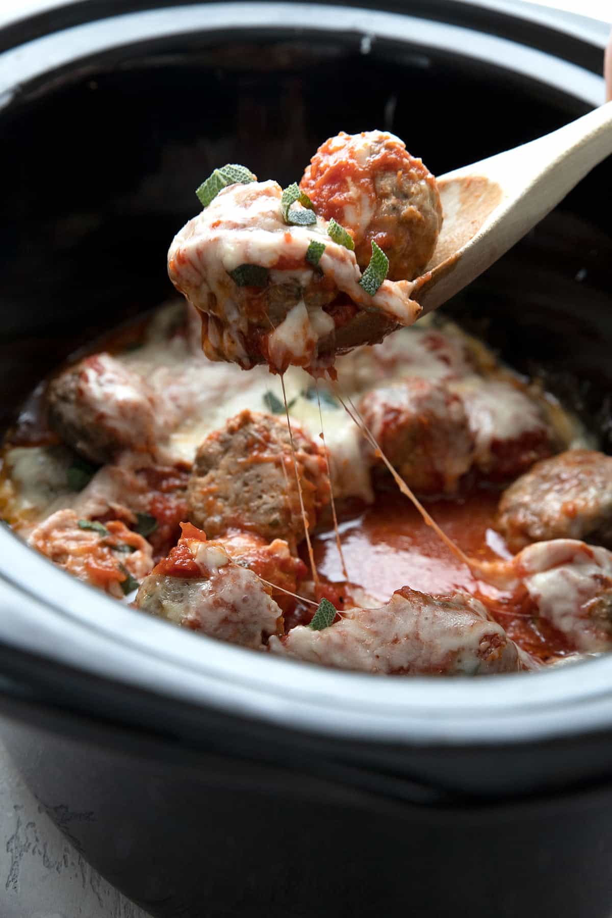 A wooden spoon lifting some keto meatball casserole out of a slow cooker.
