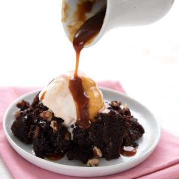 Pouring sugar free caramel sauce over a plate of keto brownies and ice cream.