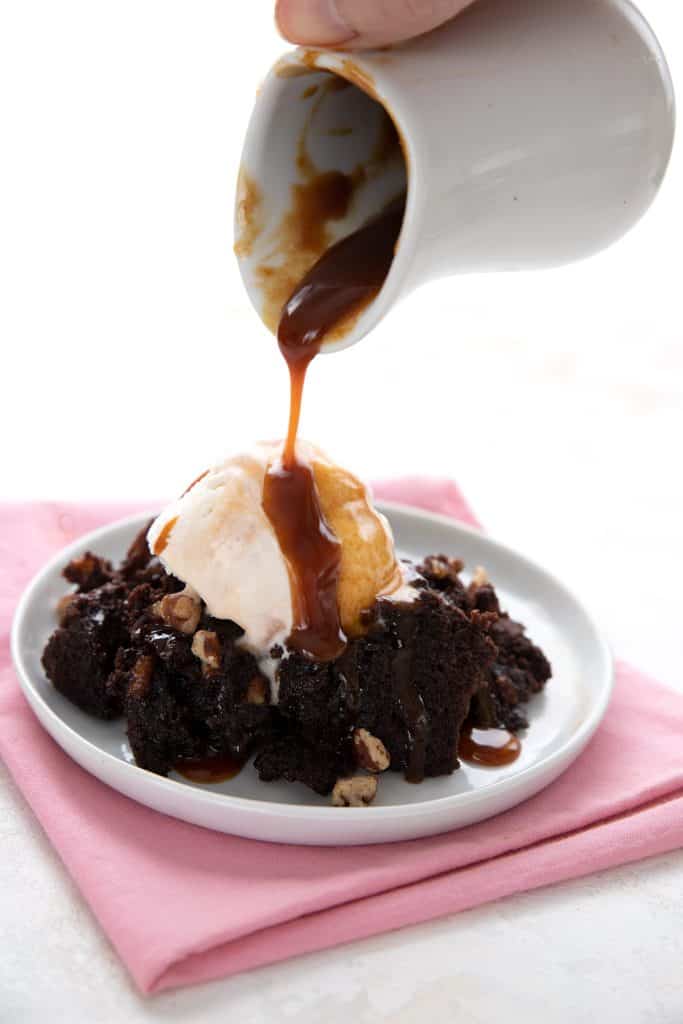 Pouring sugar free caramel sauce over a plate of keto brownies and ice cream.