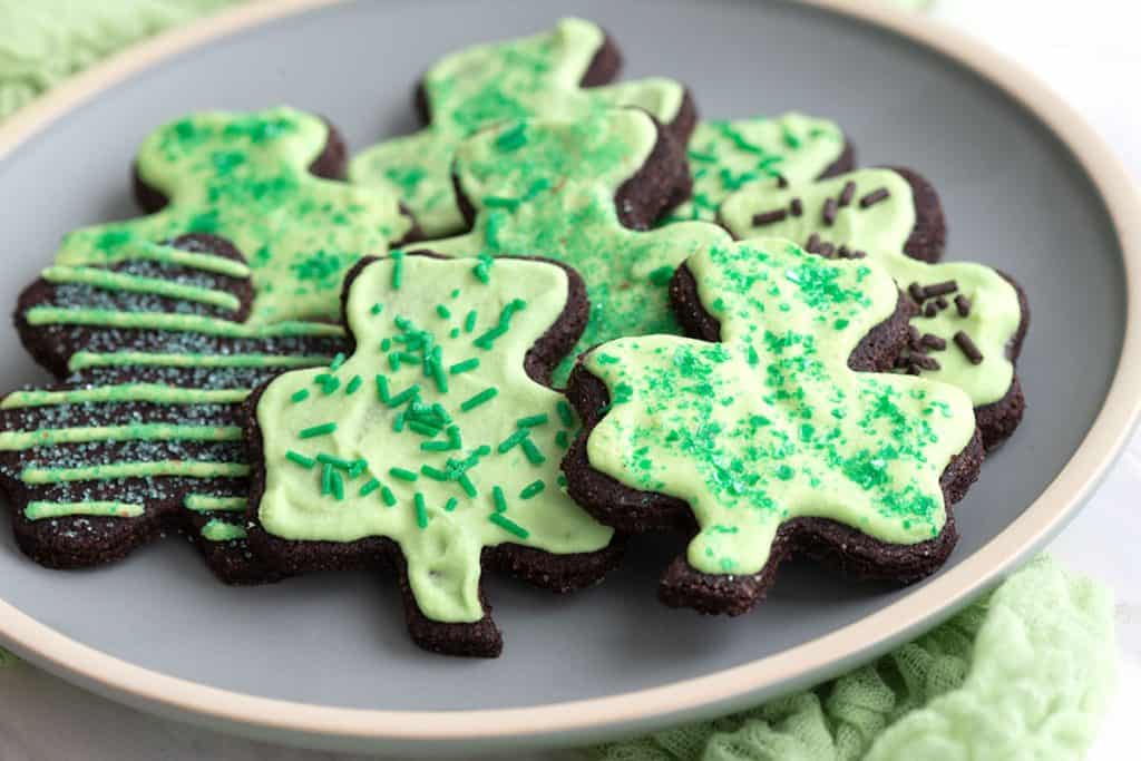 Keto shamrock sugar cookies with green frosting piled on a plate.
