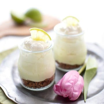 Two jars filled with keto key lime cheesecake on a pewter plate with a pink tulip.