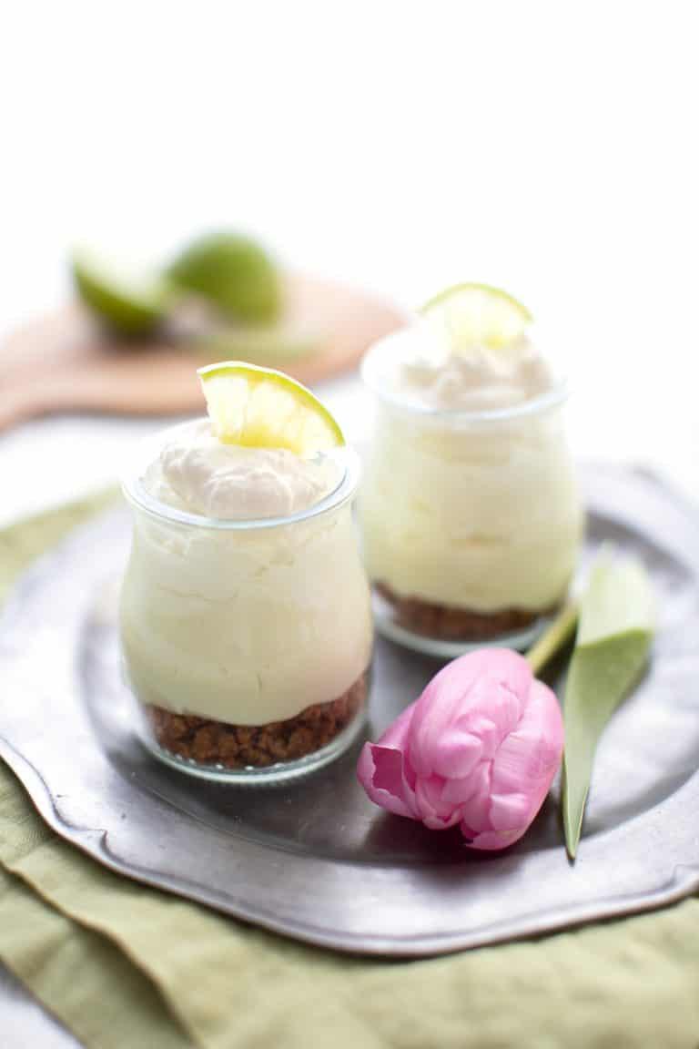 Two jars filled with keto key lime cheesecake on a pewter plate with a pink tulip.