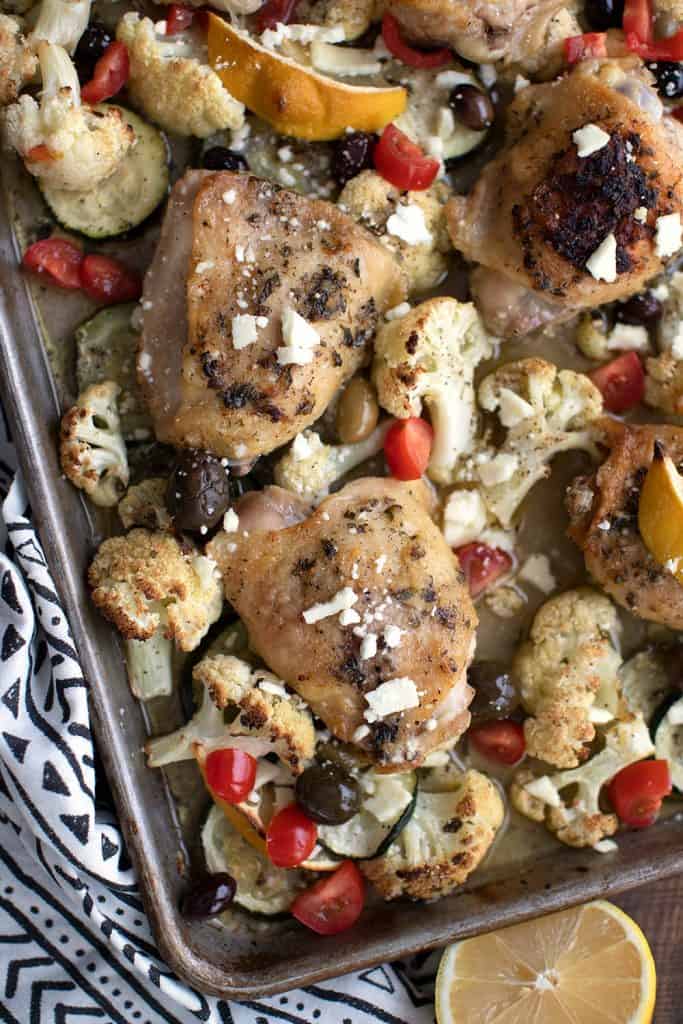 Top down image of keto Greek sheet pan chicken with cauliflower, zucchini, olives, and lemon.