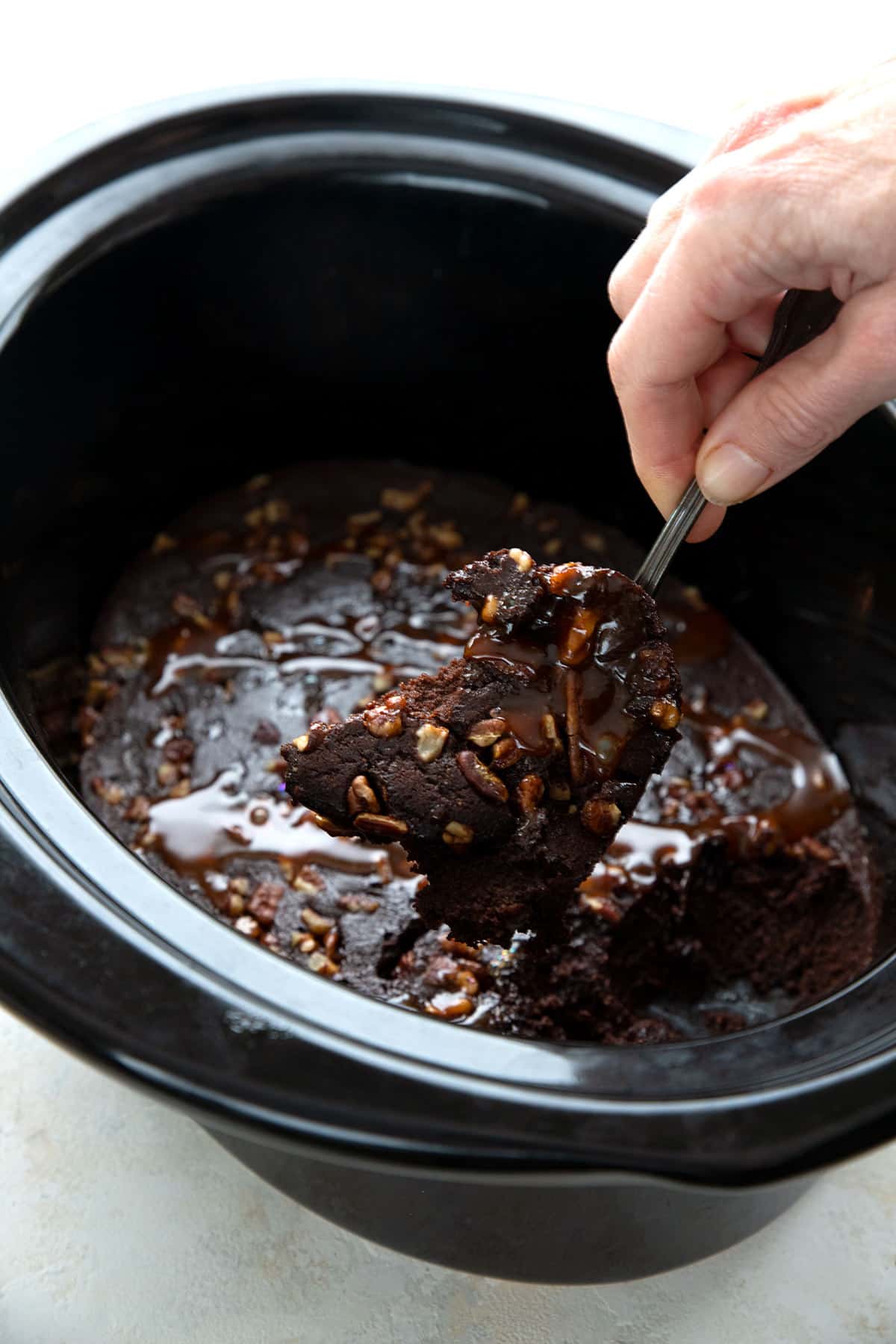 A hand scooping slow cooker brownies out of the slow cooker.
