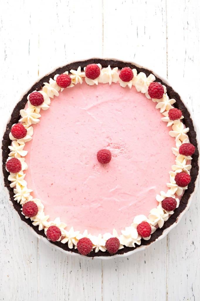 Top down image of keto raspberry tart on a white wooden table.