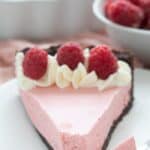 A slice of keto raspberry mousse tart on a white plate with a forkful taken out of it.