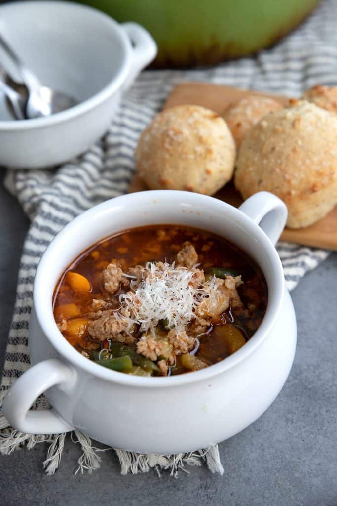 Italian sausage soup in a white bowl with keto bread rolls in the background.