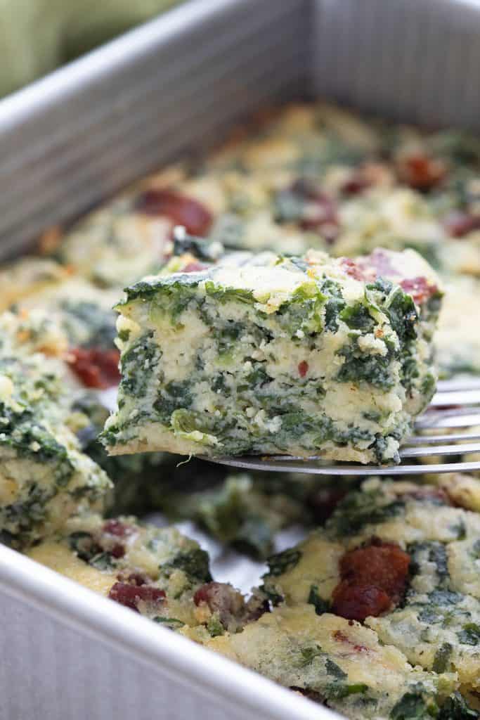 A pan of keto spinach squares with one being lifted out on a metal spatula.