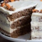 Titled image of Keto Carrot Cake on a white cake stand with a slice cut out of it.