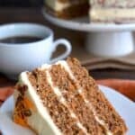 A slice of triple layer keto carrot cake with cream cheese frosting on a white plate over an orange napkin