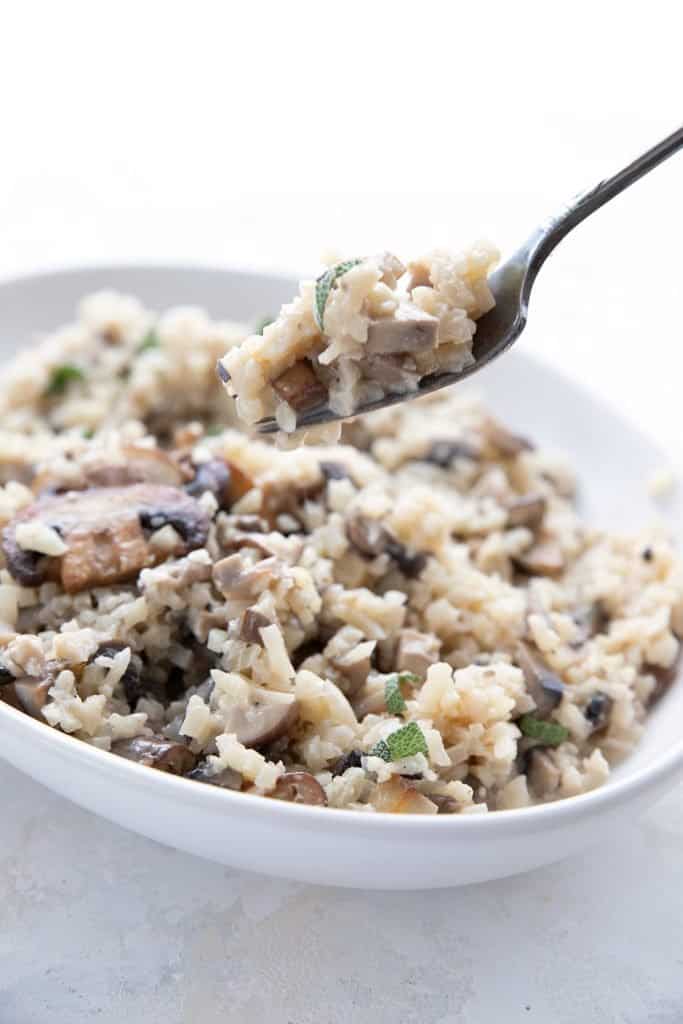 A fork lifting some keto risotto out of a white bowl.