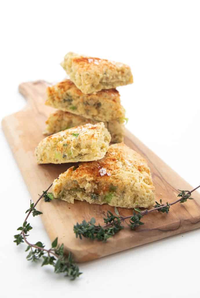 A wooden cutting board with a pile of savory keto scones, with two fresh sprigs of thyme.