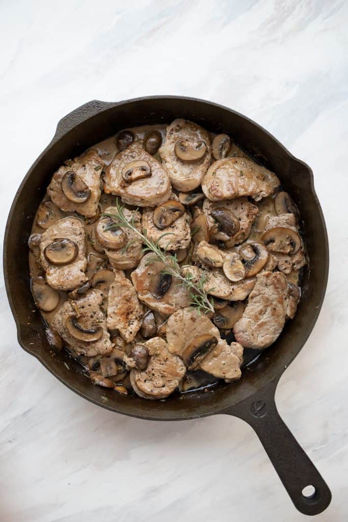 Top down image of pork medallions with mushrooms and rosemary in a cast iron pan.