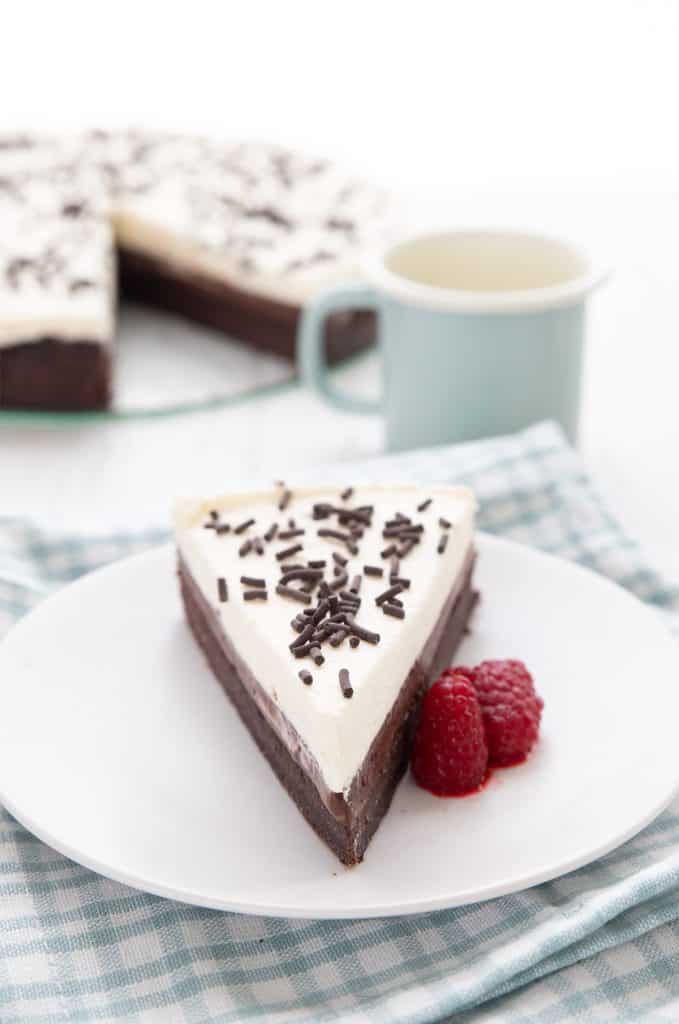A slice of keto mississippi mud pie sits on a white plate with raspberries, and the rest of the pie in the background.