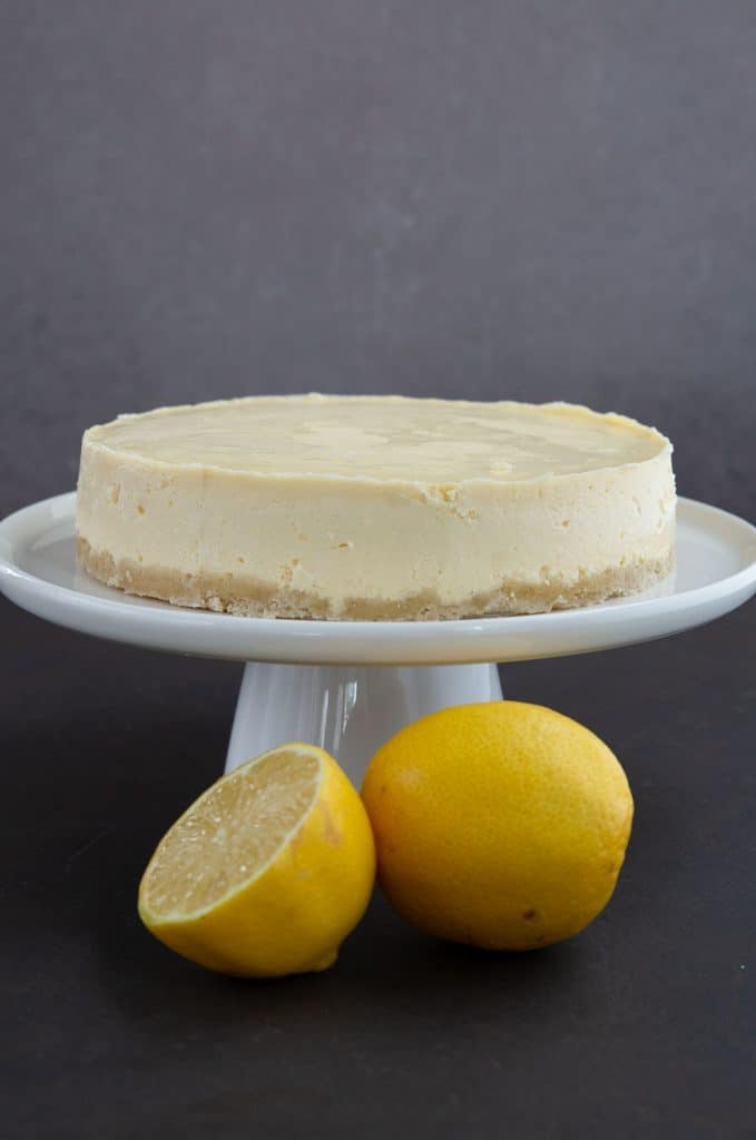 Keto Instant Pot Lemon Cheesecake on a white cake platter with a lemon and half a lemon in the foreground.
