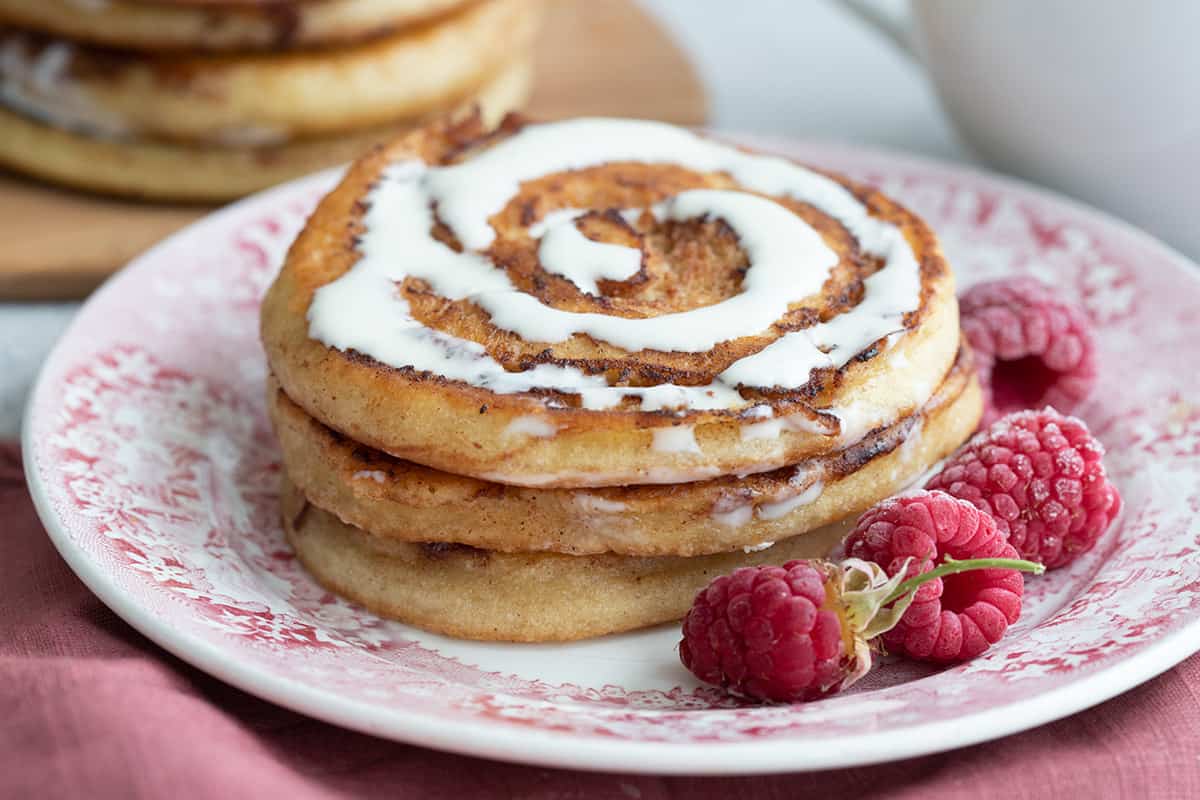 Close up shot of keto cinnamon roll pancakes on a plate with raspberries.