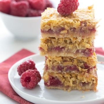 A stack of keto raspberry coconut bars on a white plate with some raspberries.