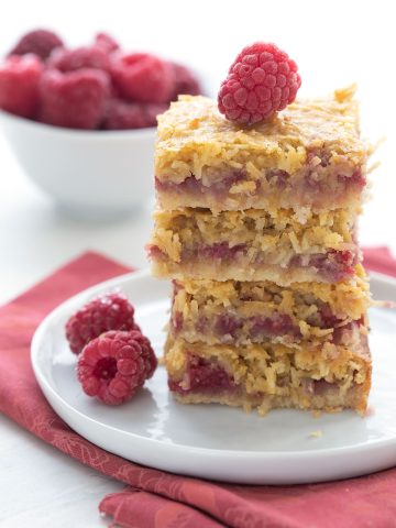 A stack of keto raspberry coconut bars on a white plate with some raspberries.