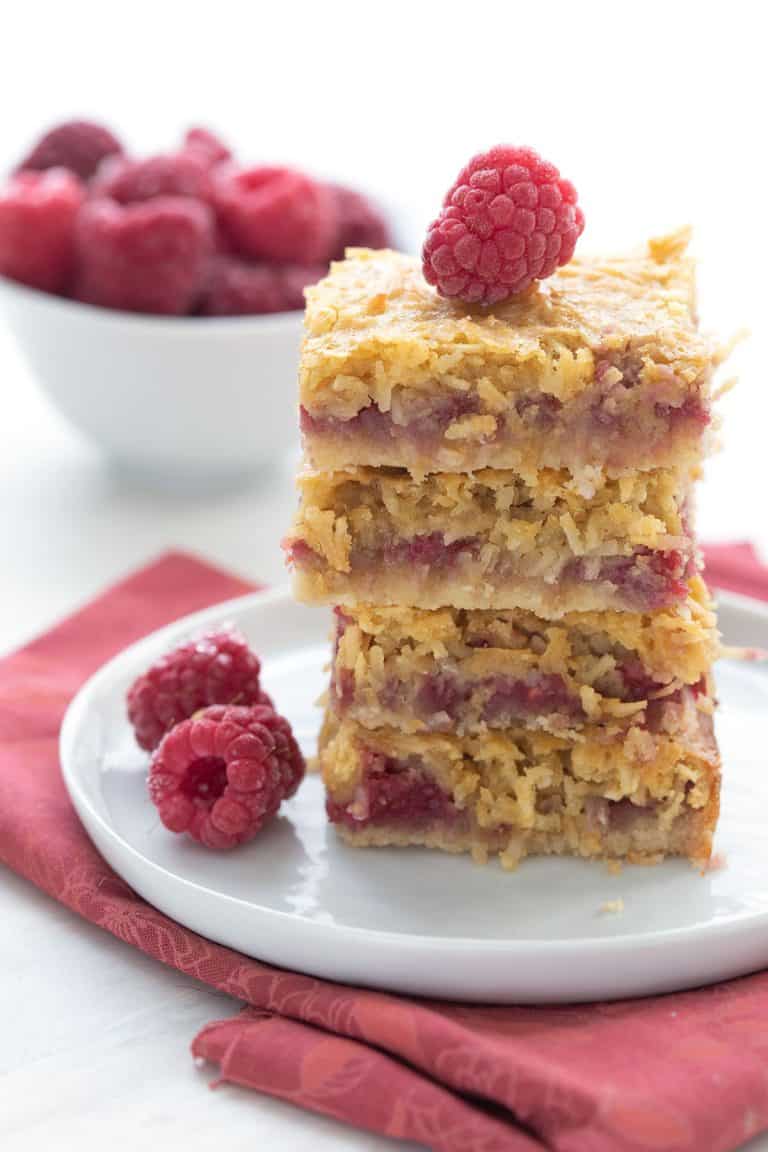 A stack of keto raspberry coconut bars on a white plate with some raspberries.